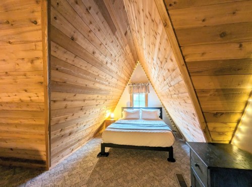 Cozy bedroom with an A-frame design, featuring wooden walls, a double bed, and soft lighting.