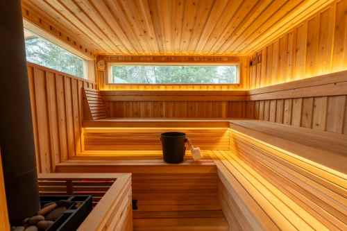 A wooden sauna interior with benches, soft lighting, and a bucket, creating a warm and relaxing atmosphere.