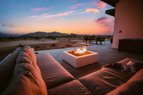 Cozy outdoor seating with a fire pit, overlooking a desert landscape at sunset.