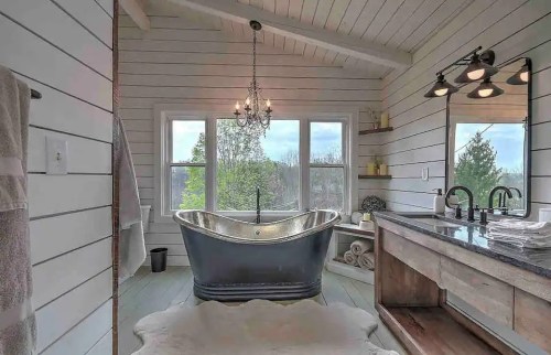A stylish bathroom featuring a freestanding tub, chandelier, and large windows with a view, accented by wooden decor.