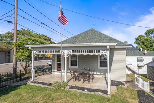 A charming house with a front porch, American flag, and outdoor seating area surrounded by greenery.