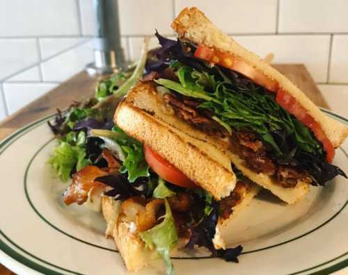 A stacked sandwich with layers of lettuce, tomato, and bacon, served on a plate with a side of mixed greens.