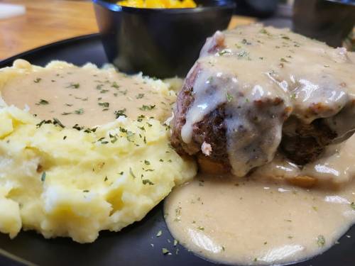 A plate of meatloaf topped with gravy, served with creamy mashed potatoes and a side of macaroni and cheese.