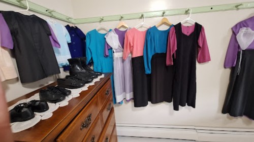 A clothing rack displays various dresses and outfits, with black shoes on a dresser in the foreground.