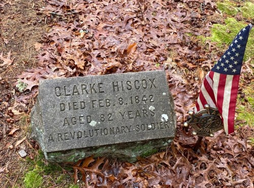 Gravestone of Clarke Hiscox, Revolutionary War soldier, died Feb. 8, 1842, aged 82, with a small American flag nearby.