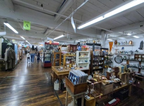 A spacious antique store filled with various vintage items, shelves, and shoppers exploring the aisles.