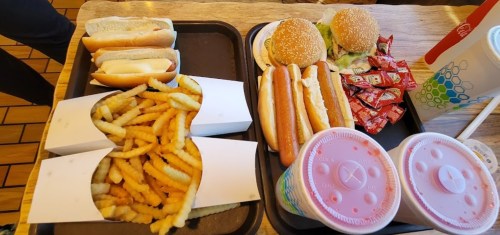 A tray with two burgers, hot dogs, fries, and two drinks, accompanied by ketchup packets.