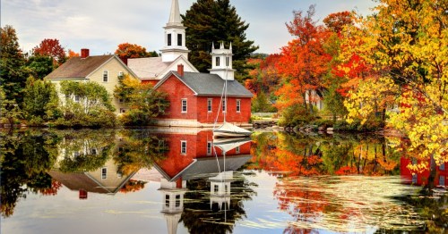 A serene autumn scene with a red church and colorful trees reflected in calm water.
