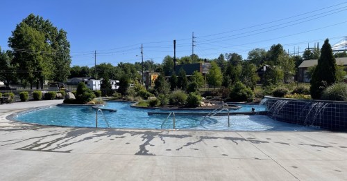 A serene outdoor pool surrounded by greenery, with gentle waterfalls and clear blue skies above.
