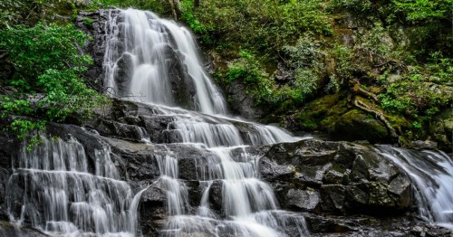 A serene waterfall cascading over rocky terrain, surrounded by lush green foliage.