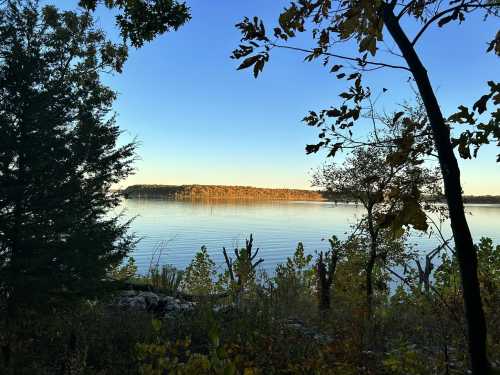 A serene lake view framed by trees, reflecting a clear blue sky and autumn foliage on the opposite shore.