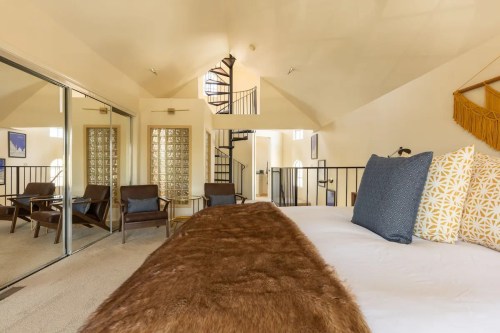 Cozy bedroom with a fur throw, large windows, and a spiral staircase leading to an upper level.