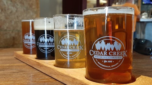 A wooden flight board holds four glasses of different beers from Cedar Creek Brewing Company.