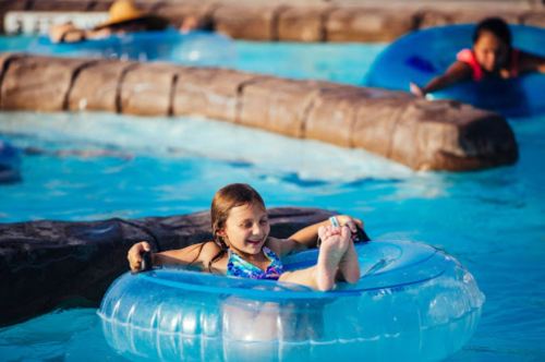 A young girl relaxes in a clear inner tube in a pool, smiling as she enjoys the water. Other children float nearby.