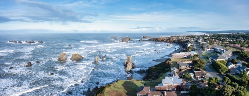 A panoramic view of a coastal town with rocky shores, waves crashing, and a clear blue sky.