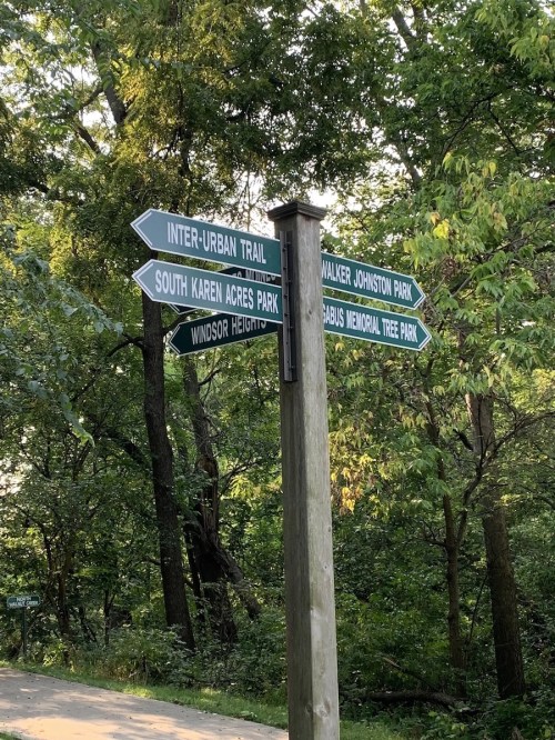 Signpost with multiple directional arrows pointing to various parks and trails in a wooded area.