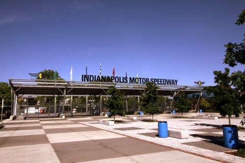 Entrance to the Indianapolis Motor Speedway, featuring flags and a clear blue sky.