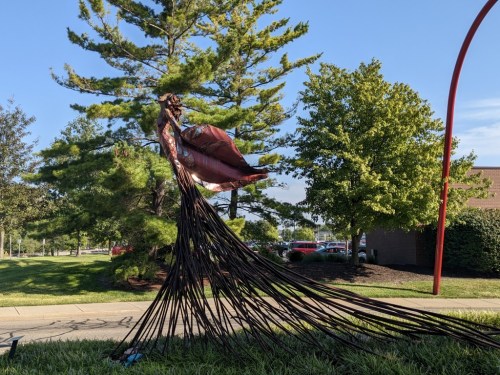 A large, artistic sculpture of a flowing dress made from metal wires, surrounded by trees and grass.