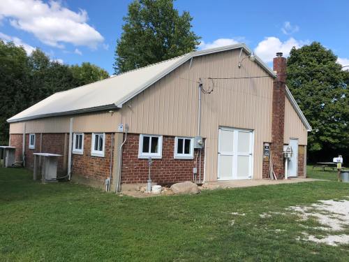 A large barn with a metal roof and brick walls, surrounded by green grass and trees under a blue sky.