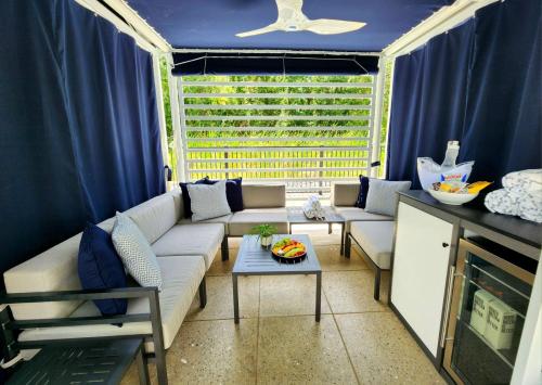 A cozy outdoor seating area with a table, fruit bowl, and curtains, surrounded by greenery.