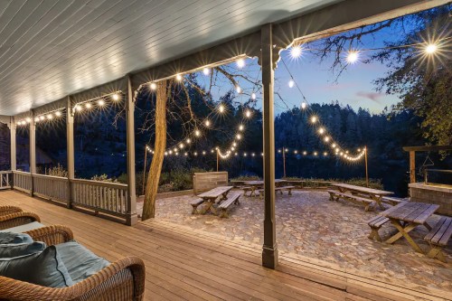 A cozy porch with string lights overlooking a serene outdoor area with picnic tables and a lake at dusk.