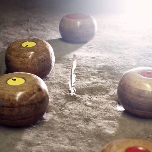 A close-up of wooden bowling balls with yellow and red markings, arranged around a feather on a textured surface.