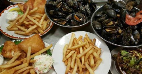 A spread of fried fish, crispy fries, mussels, and coleslaw on plates, showcasing a seafood feast.
