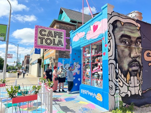 A colorful café exterior with a mural and people gathered outside, featuring vibrant decorations and a playful atmosphere.