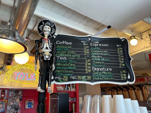 A colorful menu board featuring coffee and espresso options, with a skeleton decoration hanging above.