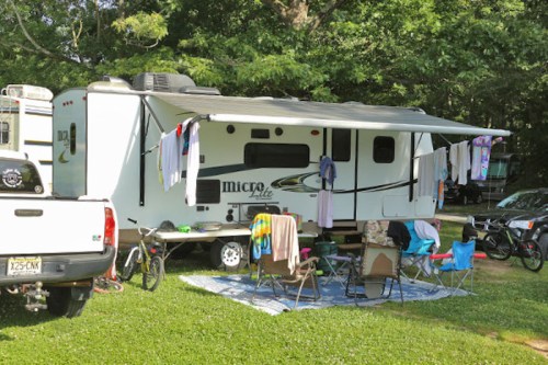 A parked camper with clothes hanging on a line, surrounded by chairs and a grassy area.