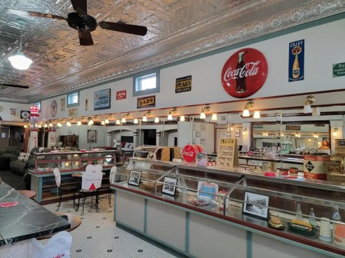 A vintage diner interior with retro decor, Coca-Cola signs, and a display case filled with desserts.