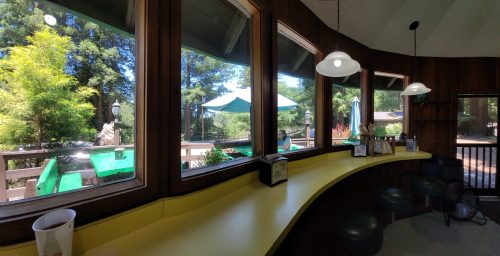A cozy interior with a yellow counter and large windows overlooking a green outdoor area with umbrellas and trees.