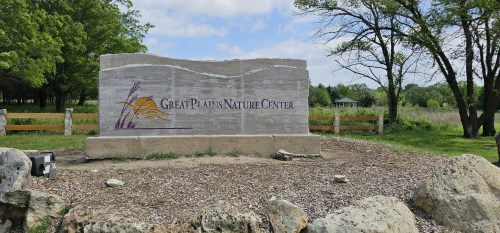 Sign for Great Plains Nature Center, surrounded by greenery and rocks, with a gazebo visible in the background.