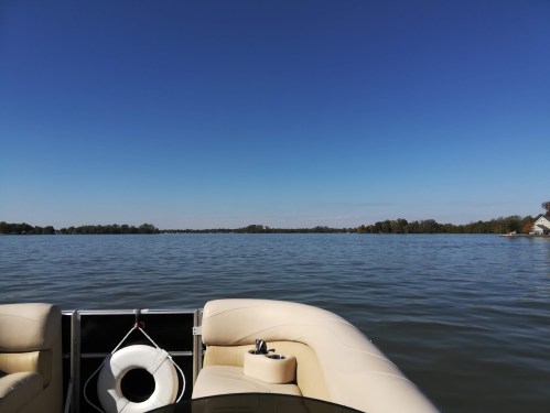 View from a boat on a calm lake, with clear blue skies and trees lining the distant shore.