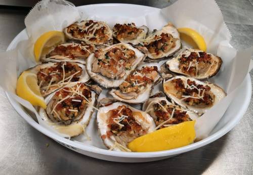 A platter of baked oysters topped with breadcrumbs and herbs, garnished with lemon wedges.