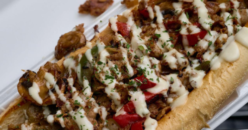 A loaded sandwich with grilled meat, peppers, and drizzled sauce, served on a toasted hoagie roll.