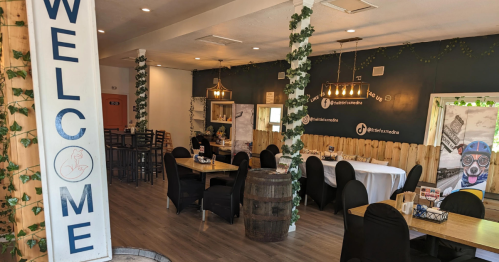 Cozy restaurant interior with wooden tables, black chairs, greenery decor, and a welcoming sign.