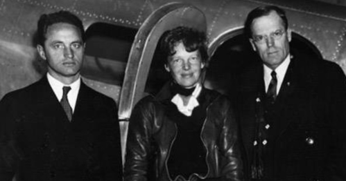 Three people stand in front of an airplane, dressed in formal and aviation attire, smiling for the camera.