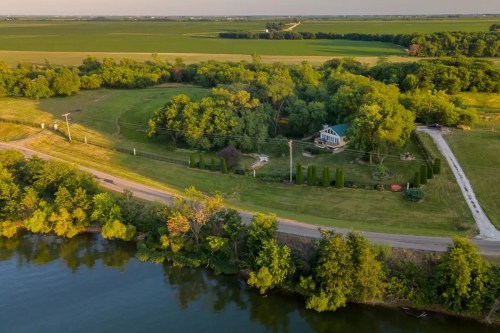 Aerial view of a lush green landscape with a house near a river and a winding road surrounded by trees.