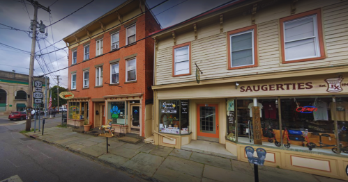 A street view of two historic buildings with shops, one featuring a sign that says "Saugerties" and outdoor seating.