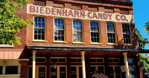 Historic brick building with large windows, featuring the sign "Biedenharn Candy Co." and an American flag.