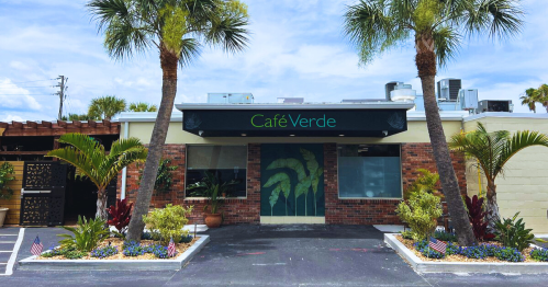 Exterior of Café Verde, featuring palm trees, colorful plants, and a welcoming entrance with a sign above.