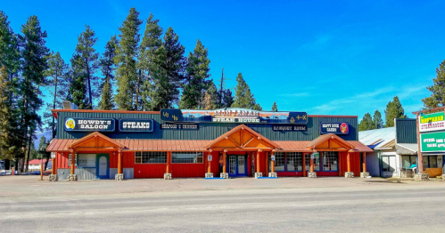 A rustic steakhouse with a red facade, surrounded by tall trees and a clear blue sky.