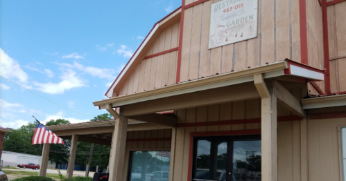 A rustic restaurant building with a sign and an American flag outside, under a blue sky with scattered clouds.