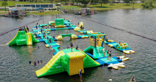 A colorful inflatable water park with various structures, surrounded by people swimming and enjoying the water.