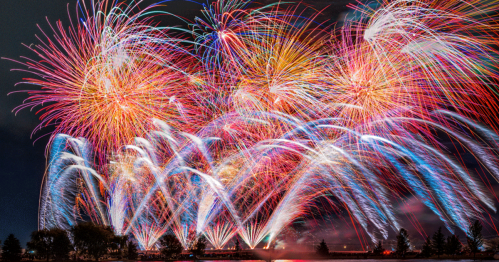 Colorful fireworks burst in the night sky, creating a vibrant display over a dark landscape.