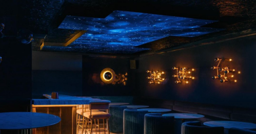 A dimly lit lounge with a starry ceiling, stylish seating, and modern lighting fixtures on the walls.