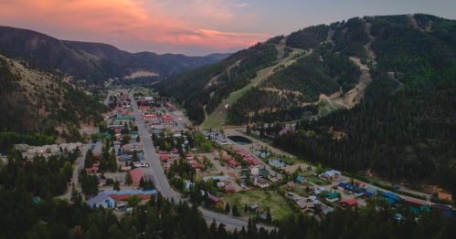 Aerial view of a small town nestled in a valley, surrounded by mountains and forests at sunset.