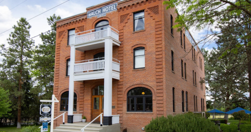 Historic Balch Hotel, a three-story brick building with balconies, surrounded by greenery and a blue sky.