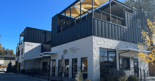 Modern restaurant building with a rooftop patio, featuring large windows and a clean, minimalist design.
